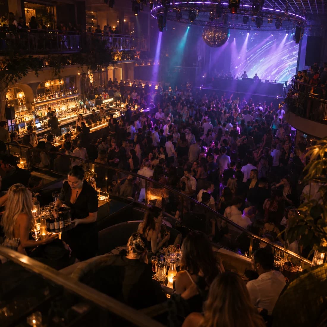 A packed crowd faces a stage under the light rig, seen from the balcony